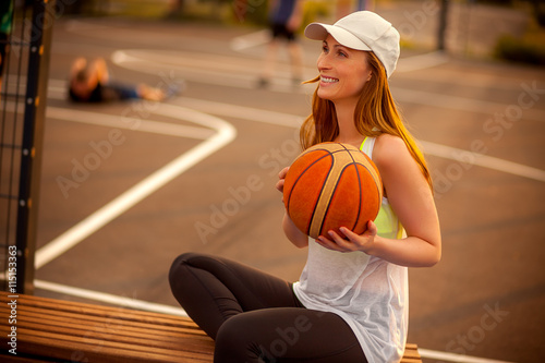 Frau sitzt auf einer Bank und hält ein Basketball