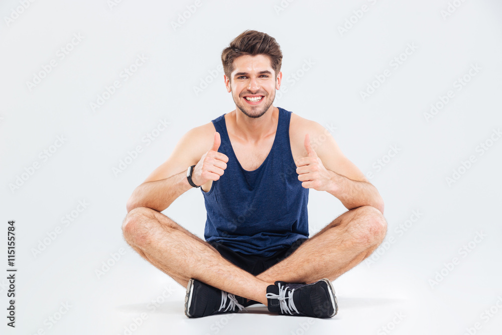 Happy young fitness man sitting and showing thumbs up Happy young fitness man sitting and showing thumbs up