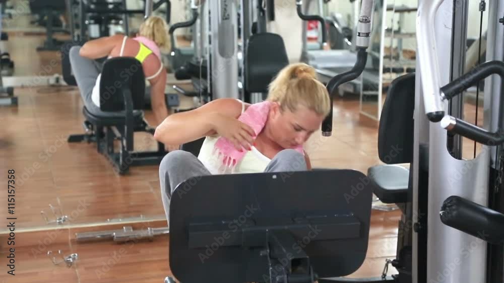 Blonde woman drying sweat with a towel and drinking water in gym Blonde woman drying sweat with a towel and drinking water in gym