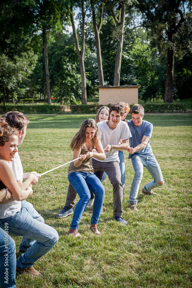 Young friends playing tug with rope in a park during the summer break from studies