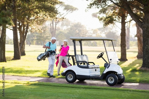 Smiling mature golfer couple by golf buggy