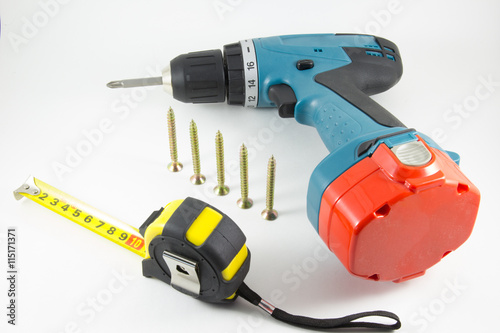 Cordless screwdriver, screws and tape measure on a white background