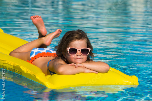 little girl swims in a pool in an yellow life preserver