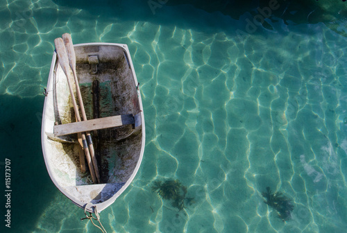 Quadro su tela Looking down from above on a small rowing boat with its oars resting inside and tethered to a harbour wall on a calm, green sea