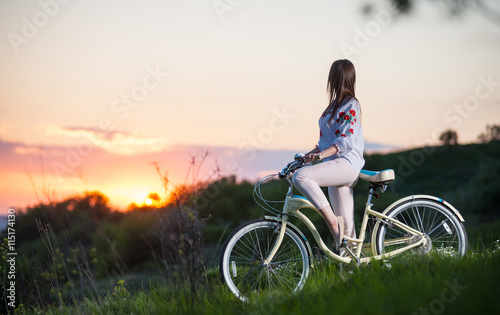 Beautiful sunset and female in Ukrainian embroidery with retro bicycle enjoying them. Blurred background