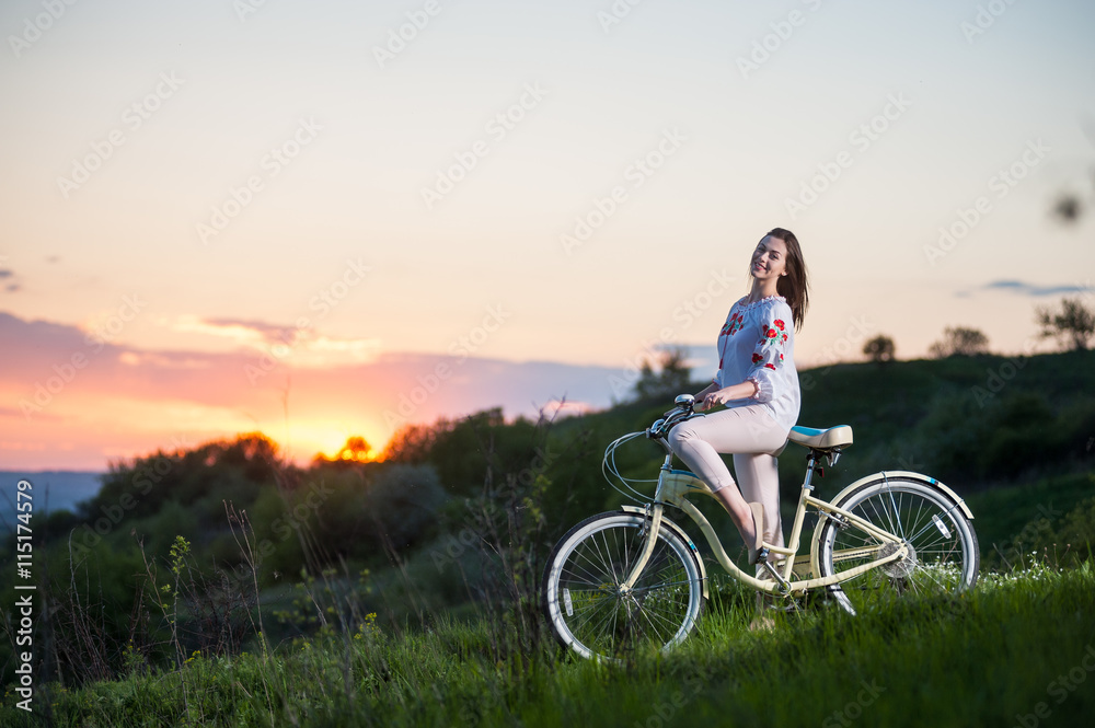 Beautiful sunset and happy girl in Ukrainian embroidery with bike enjoying them. Blurred background Beautiful sunset and happy girl in Ukrainian embroidery with bike enjoying them. Blurred background
