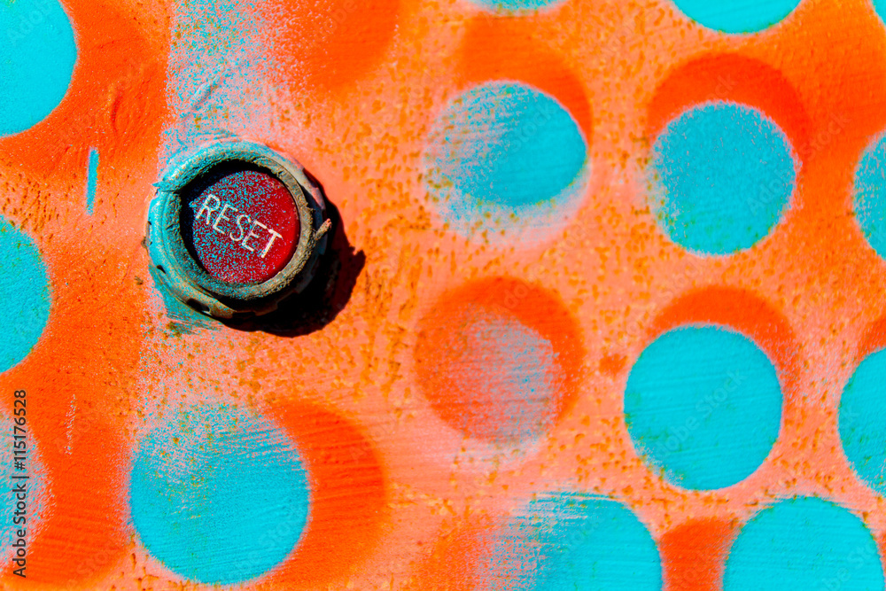 red reset button on wall painted with blue and orange dots - obrazy, fototapety, plakaty 