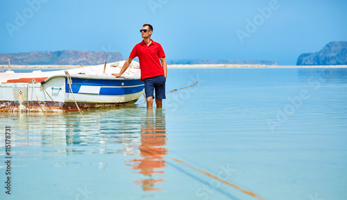 man standing in the sea near the boat. man wearing in red polo shirt and sunglass