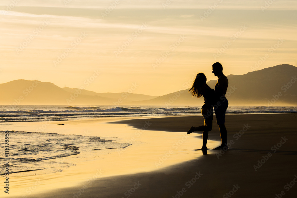 Lovers at sunset holding looking at each other on a beach silhouettes