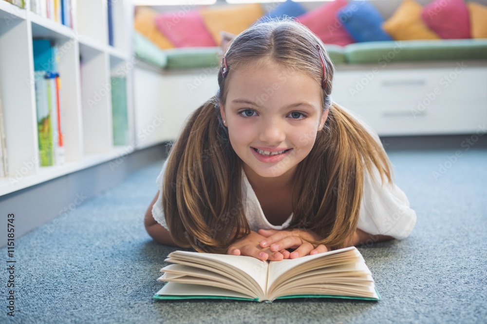 Schoolgirl lying on floor and reading a book in library Schoolgirl lying on floor and reading a book in library