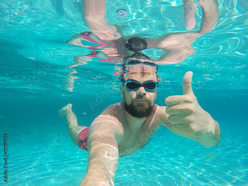 Beard man with glasses diving in a blue clean water