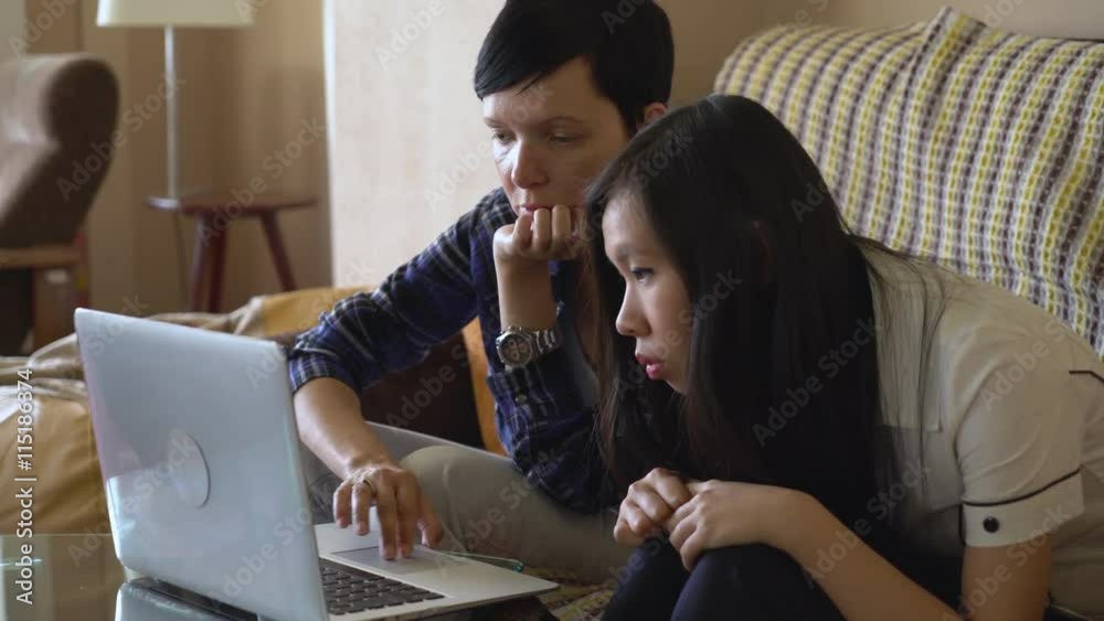 Adult caucasian woman looking at laptop explain something young asian girl. Multicultural team work with computer indoors. Vietnamese girl focus on screen. Older female shows errors that must be Adult caucasian woman looking at laptop explain something young asian girl. Multicultural team work with computer indoors. Vietnamese girl focus on screen. Older female shows errors that must be