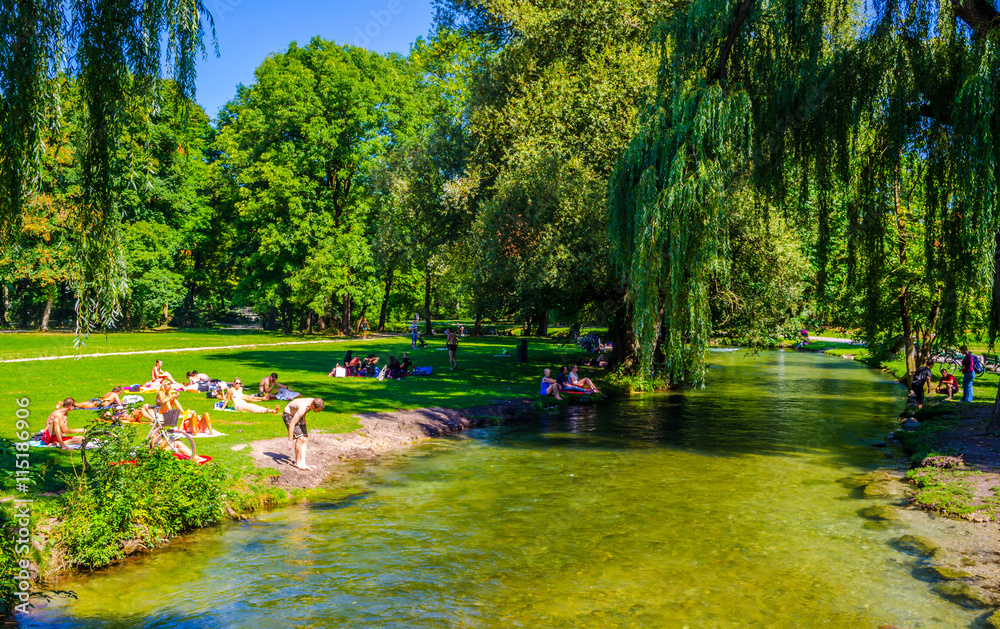 Naklejka premium People are sunbathing and having a picnic next to an artificial creeking inside of the english garden in bavarian city munich