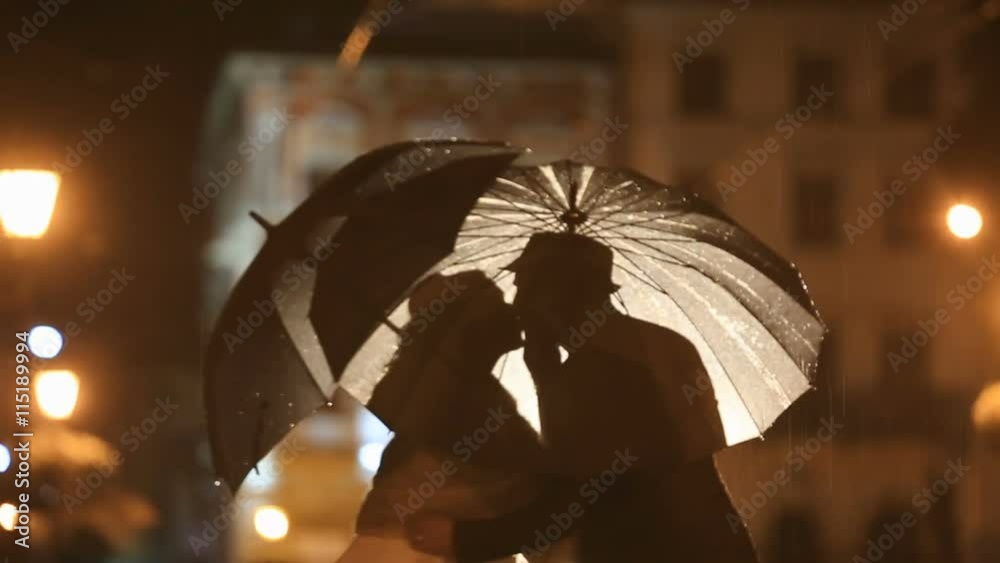 Romantic kiss under rain on night city street, hiding from rain under umbrellas. City lights show pair silhouettes in noir atmosphere