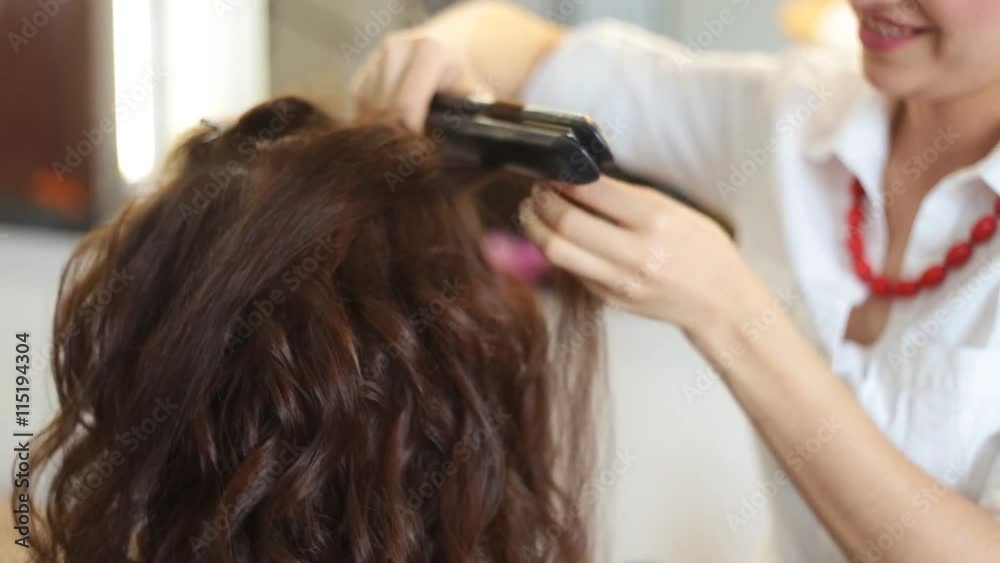 young woman and hairdresser with hair iron making hairdo at hair salon young woman and hairdresser with hair iron making hairdo at hair salon