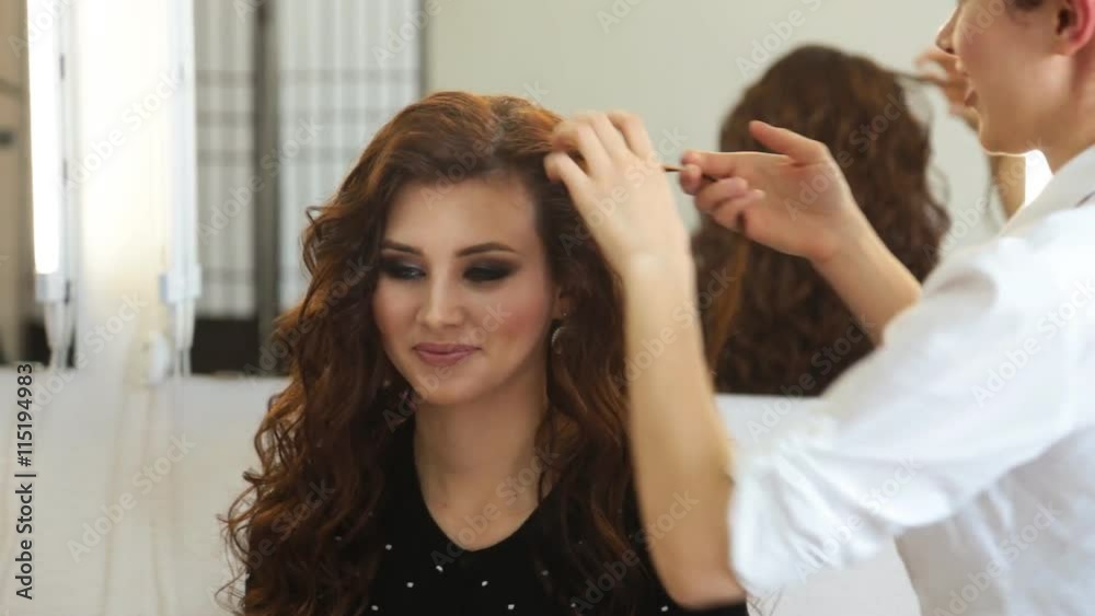 young woman and hairdresser with hair iron making hairdo at hair salon young woman and hairdresser with hair iron making hairdo at hair salon