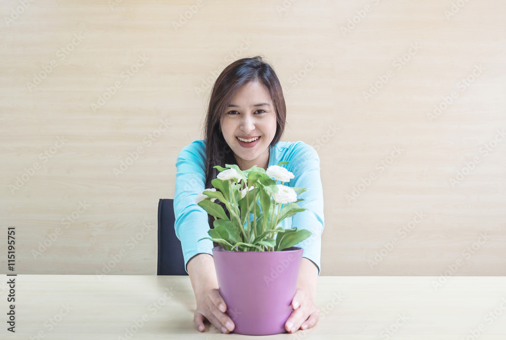 Closeup asian woman with happy face in relaxation concept with artificial white flower in purple flower pot in her hand on blurred wooden desk and wall textured background in the meeting room Closeup asian woman with happy face in relaxation concept with artificial white flower in purple flower pot in her hand on blurred wooden desk and wall textured background in the meeting room
