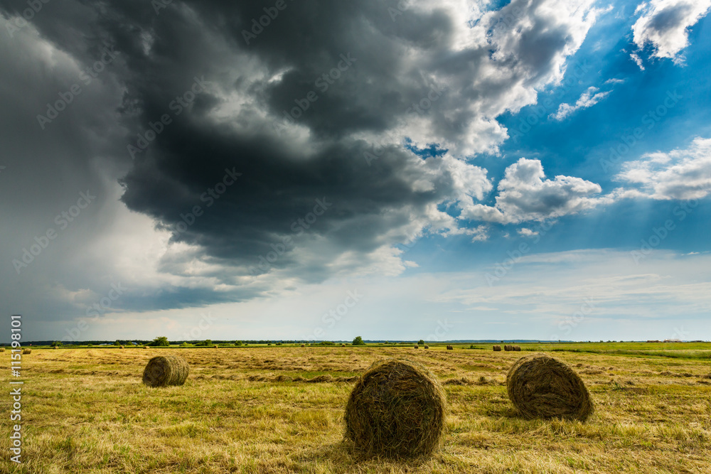 Dramatic scenery with field, storm clouds and haystacks