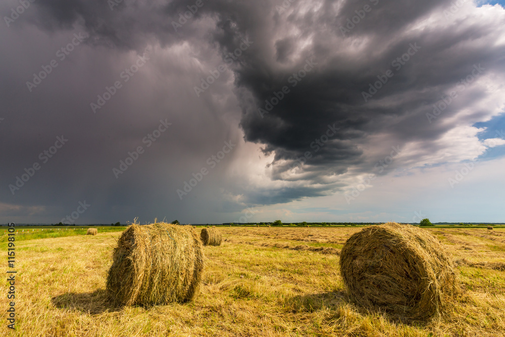 Dramatic scenery with field, storm clouds and haystacks