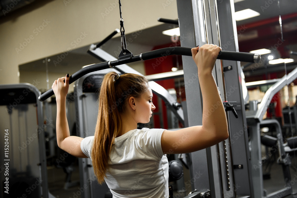 Fototapeta premium A young sportswoman working our seriously in a big gym. Training for strength of the back muscles