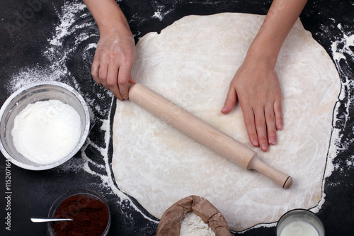 female hands rolling dough with a rolling pin on a black background