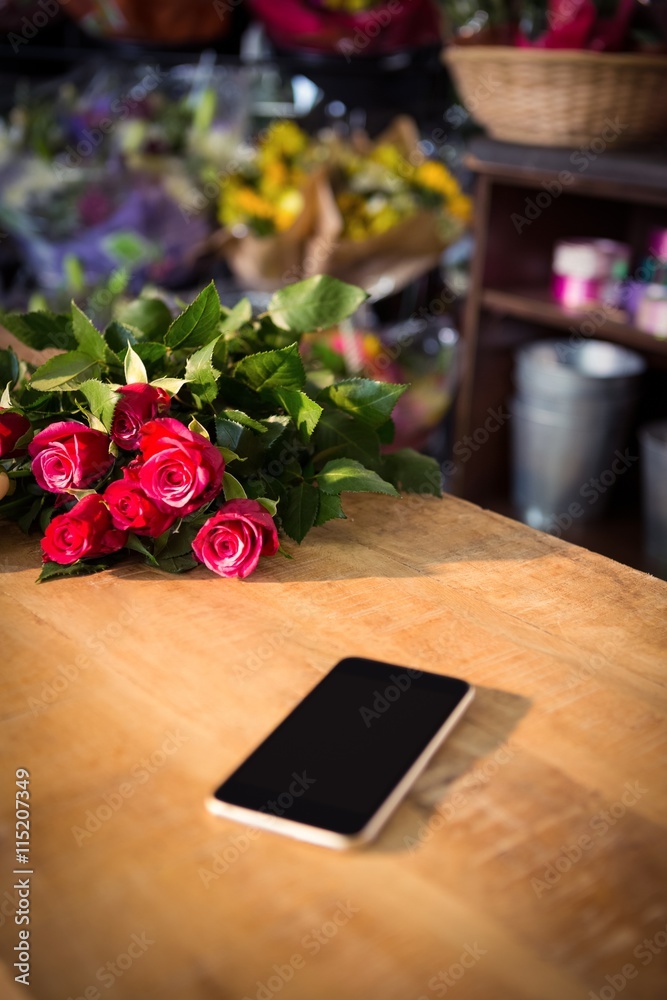 Obraz premium Bunch of red roses and smartphone on the wooden table