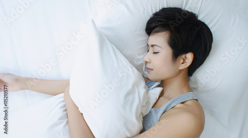 Asian woman sleeping in white bed, holding and hugging a pillow, view from above