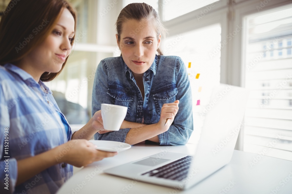 Businesswoman holding coffee cup while working with colleague Businesswoman holding coffee cup while working with colleague