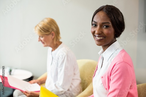 Woman smiling at camera while her colleague reading document