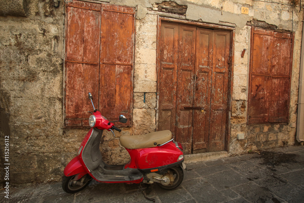 Fototapeta premium Red scooter near the old stone wall with wooden door and wondow