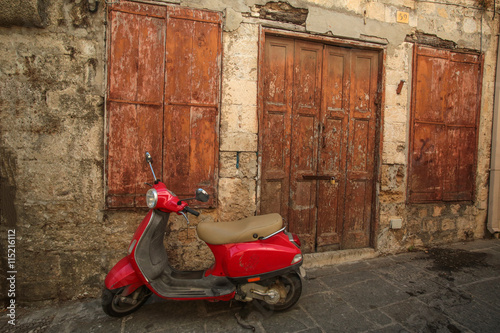 Red scooter near the old stone wall  with wooden door and wondow