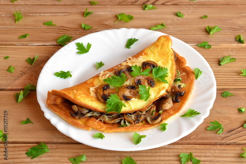 A tasty omelet with mushrooms, cheese and parsley. Stuffed omelet on a plate and on a wooden table. Eggs recipe. Quick vegetarian breakfast idea