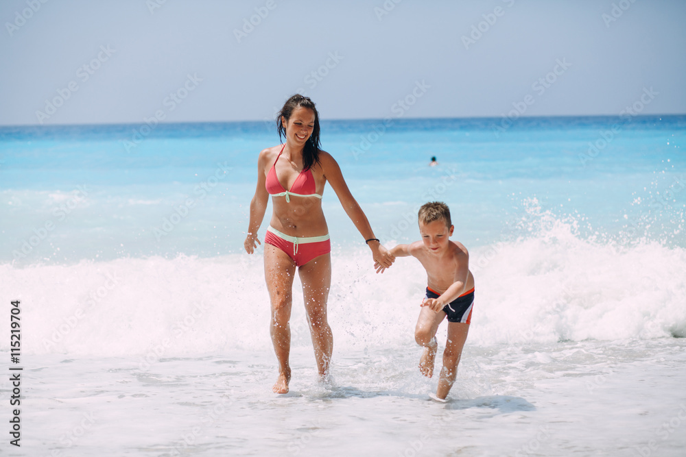 Young mother and her son enjoying in beautiful sunny tropical beach. Sea in the background.