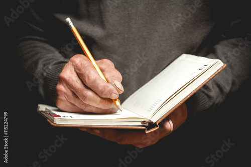 Photography An elderly man wrote in pencil in a notebook. Photo in low key
