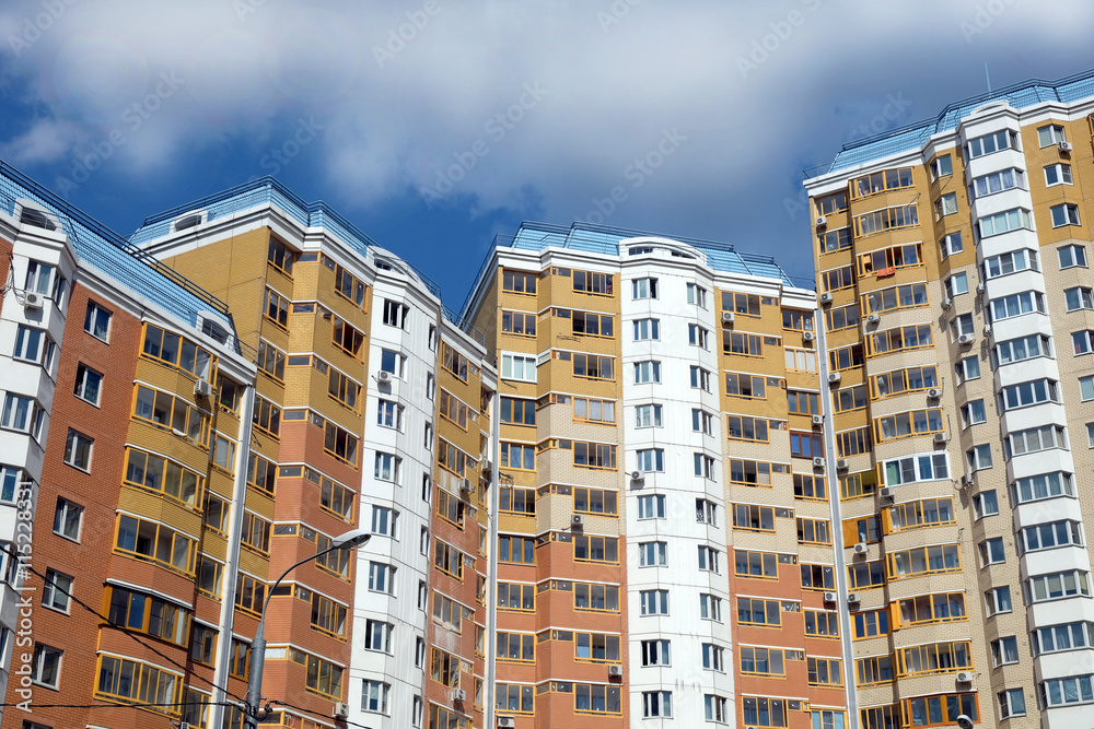 Top section of modern apartment buildings constructed from bricks over clear blue sky with white clouds on summer day