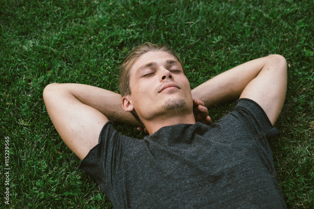 Attractive Young Man Lying with Both Hands Resting Behind his Ne - obrazy, fototapety, plakaty 