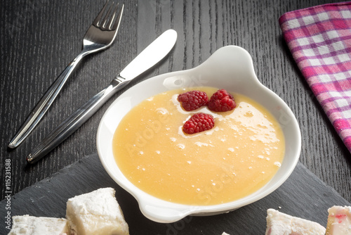 Crema pasticcera con lamponi rossi nel contenitore in ceramica su un tavolo photo