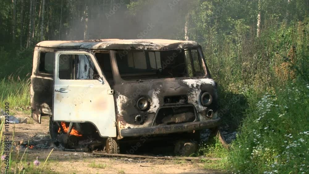 Old burning car emitting smoke in an empty summer field Old burning car emitting smoke in an empty summer field