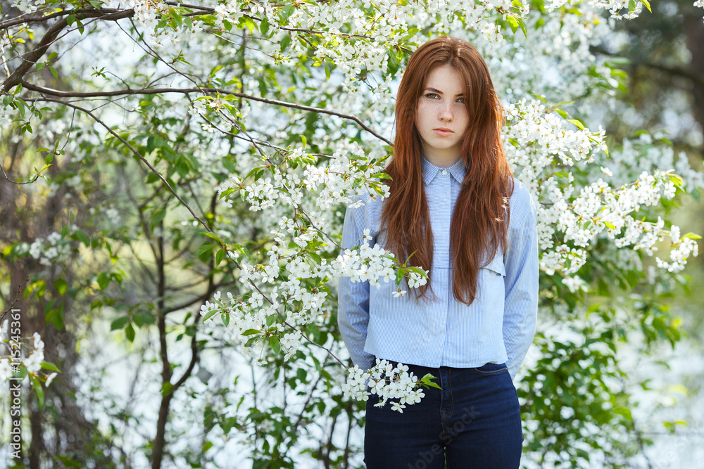 Portrait of a beautiful redhead women in shirt and jeans in blossom apple tree garden in spring time Portrait of a beautiful redhead women in shirt and jeans in blossom apple tree garden in spring time