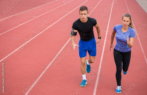 Two young athletic people running on race track. Male and female professional athletes running on athletics race track.