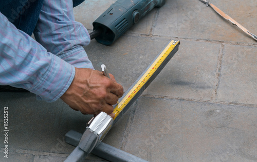 Worker measuring stainless steel railing with measuring tape in construction site 