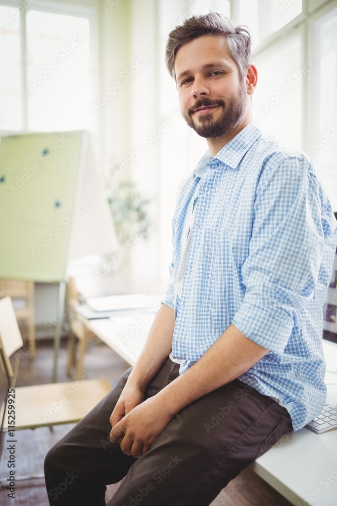 Portrait of smiling businessman sitting on desk in office Portrait of smiling businessman sitting on desk in office