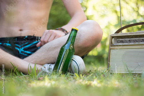 Junger Mann sitzt Radio und Bierflasche im Park photo