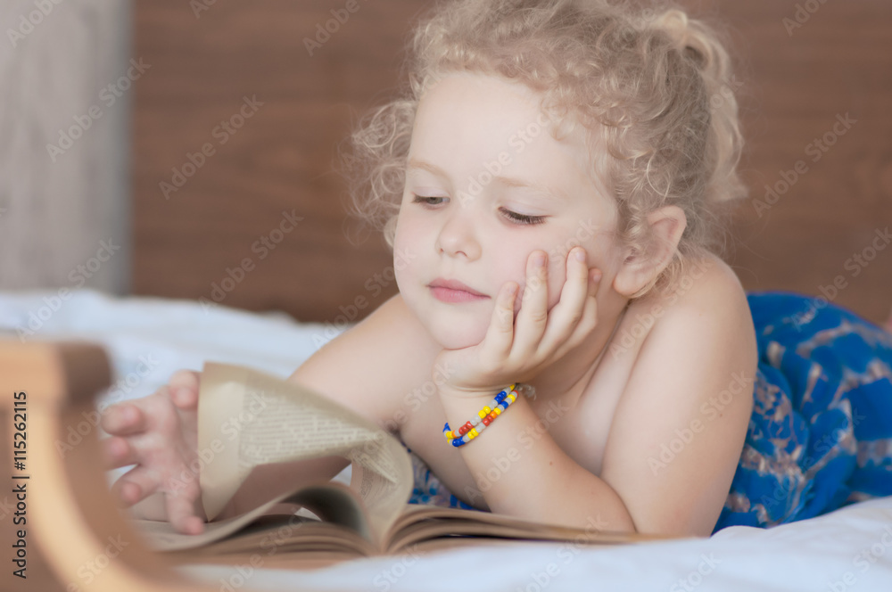 Fototapeta premium caucasian curly blonde girl reading an old vintage book with yellow sheet on a bed in the bedroom