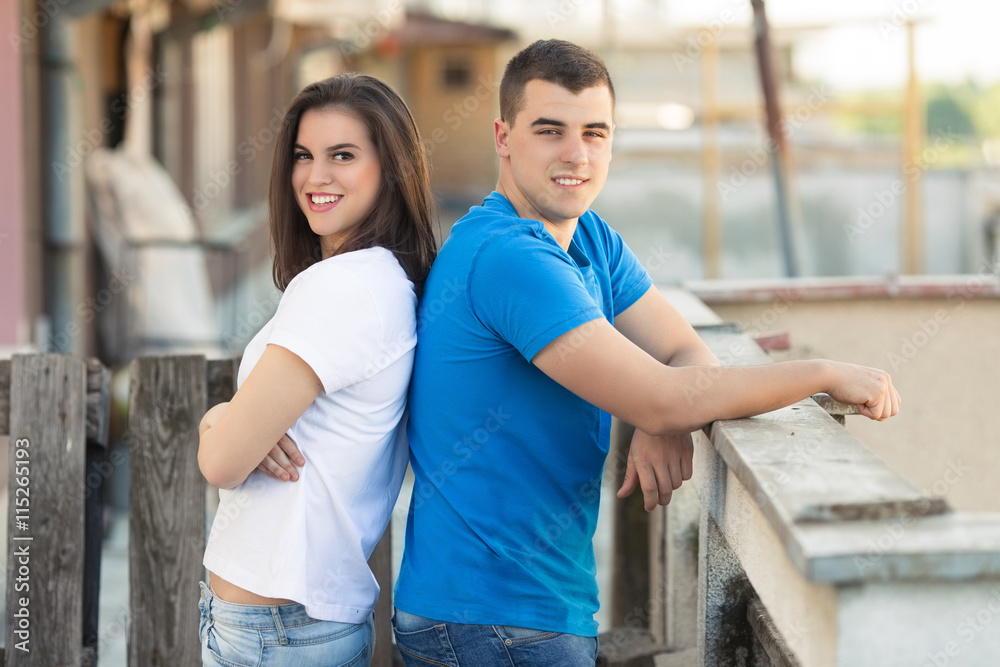 Portrait of happy young couple. Smiling young woman and man are standing back to back and looking at camera.