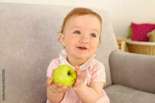 Baby with apple on sofa in ...
