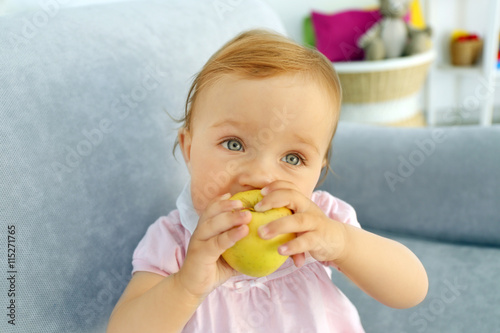 Baby with apple on sofa in ...