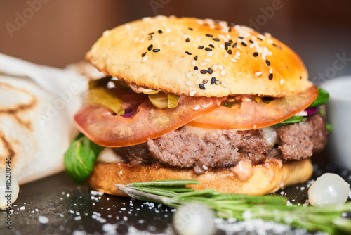 A hamburger consisting of meat patties, cheese and vegetables served on a stone Board closeup