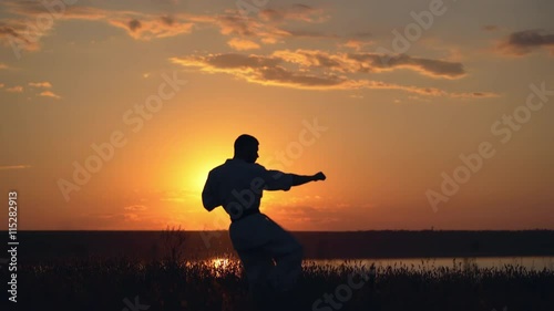 Silhouette of man training karate at sunset.
