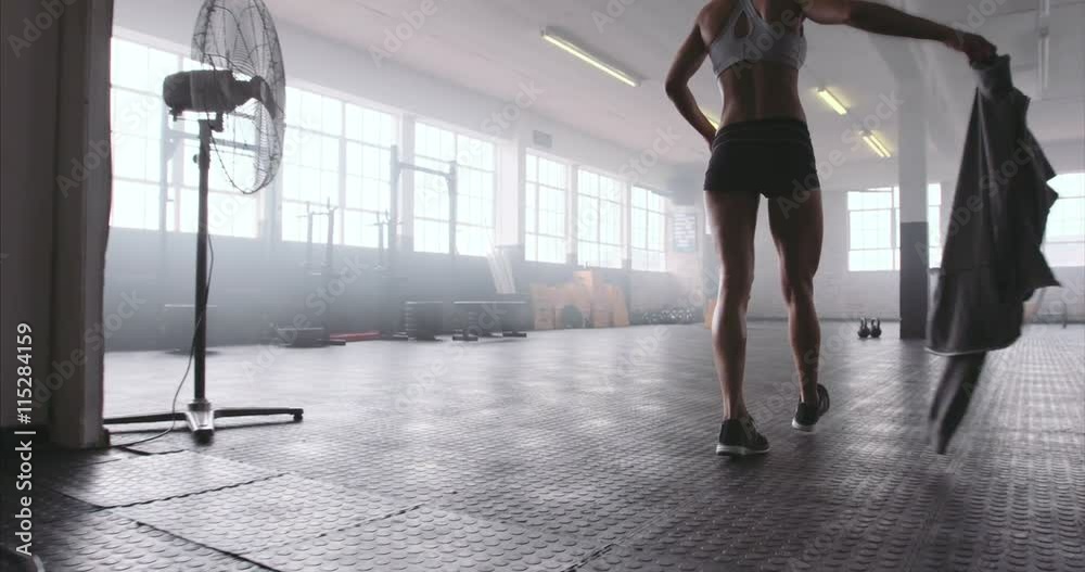 Fitness woman entering the gym, taking out her sweatshirt and picking up the kettle bell. Female athlete about the start her physical training at cross fit gym.

